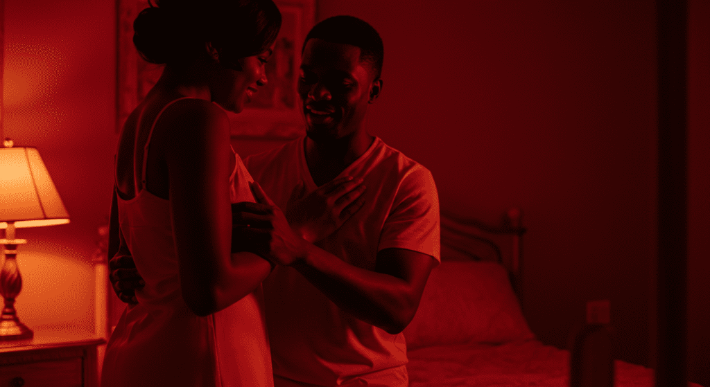 Homme noir tenant la taille d'une femme dans une chambre. L’arrière-plan est faiblement éclairé avec des tons rouges.